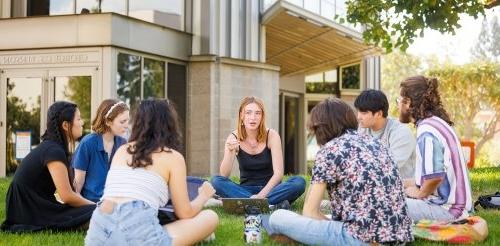 students sit on the grass in a cirle on the mounds during a study session