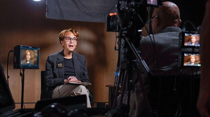 Muriel Poston talks and sits in a chair while being filmed. 