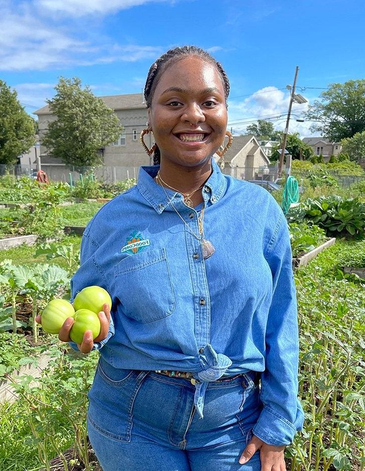 Yaquana Williams stands in a garden holding produce. 