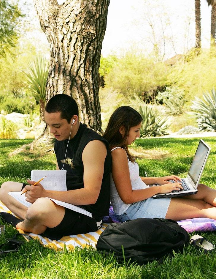 two students sit back to back while studying on the mounds